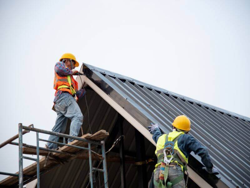 two roofers are installing a metal roof while following roofing standards