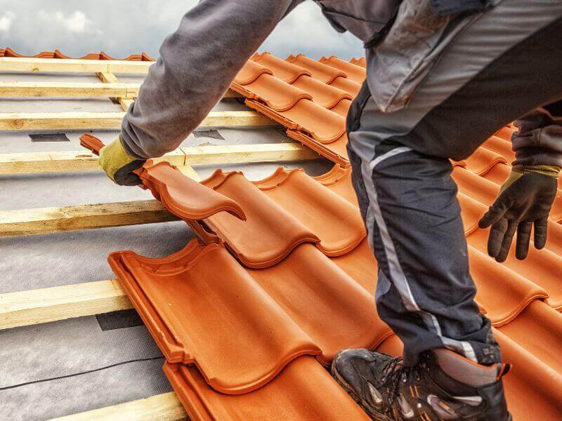 worker installing clay roof tiles on wooden frame
